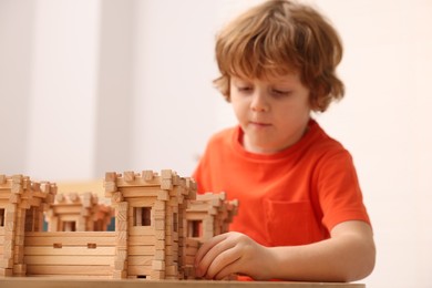 Photo of Little boy playing with wooden fortress at table in room, selective focus. Child's toy