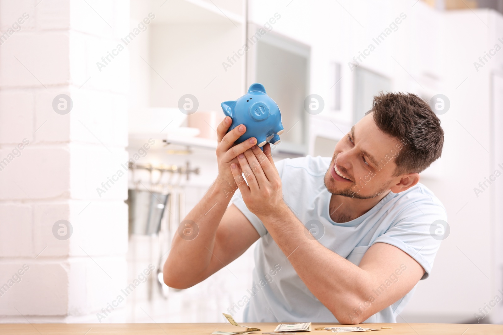 Photo of Man with piggy bank and money at home. Space for text