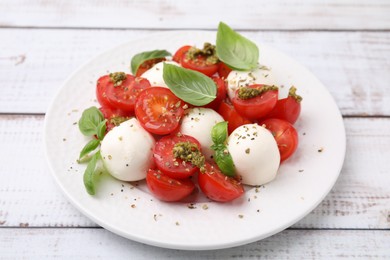 Tasty salad Caprese with tomatoes, mozzarella balls and basil on white wooden table, closeup