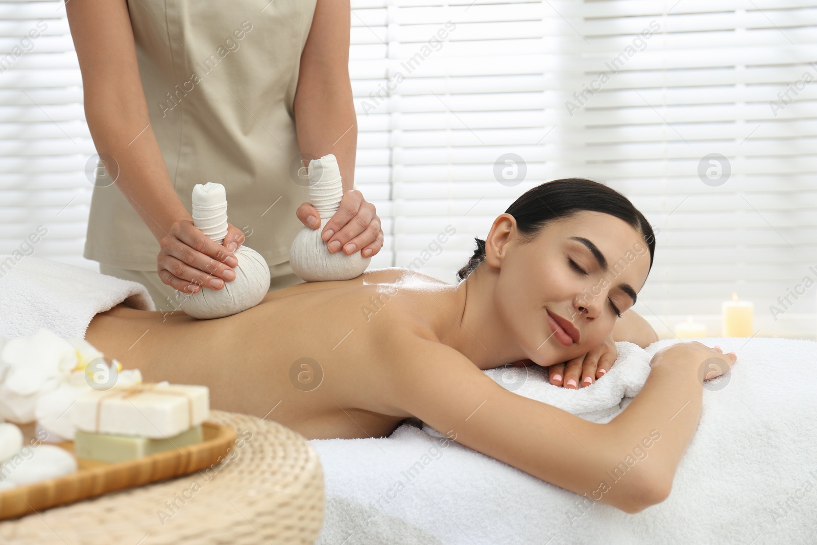 Photo of Young woman receiving herbal bag massage in spa salon