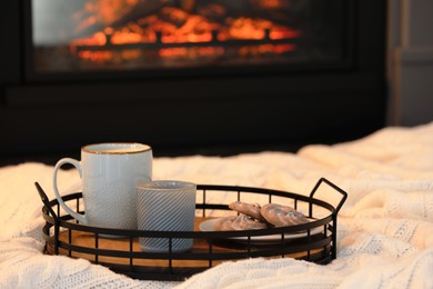 Cup of hot drink and candle on tray near fireplace at home, space for text. Cozy atmosphere