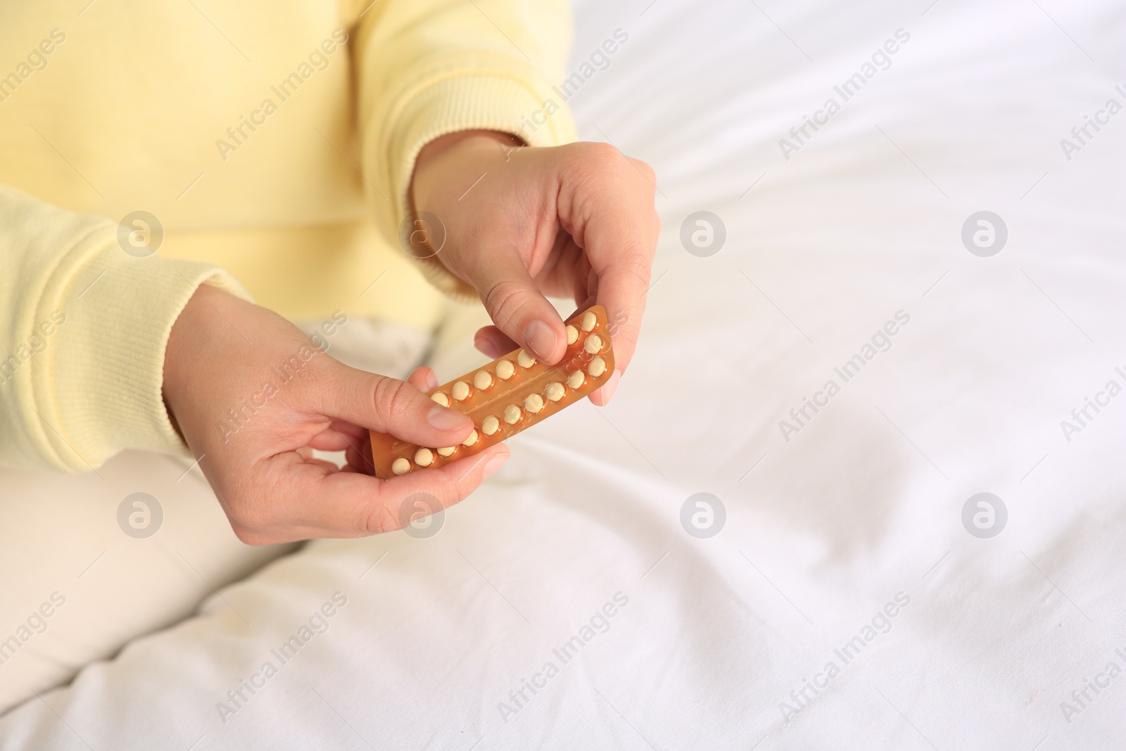 Photo of Woman taking blister of oral contraception pill in bedroom, focus on hands