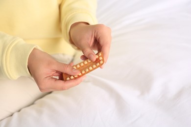 Photo of Woman taking blister of oral contraception pill in bedroom, focus on hands