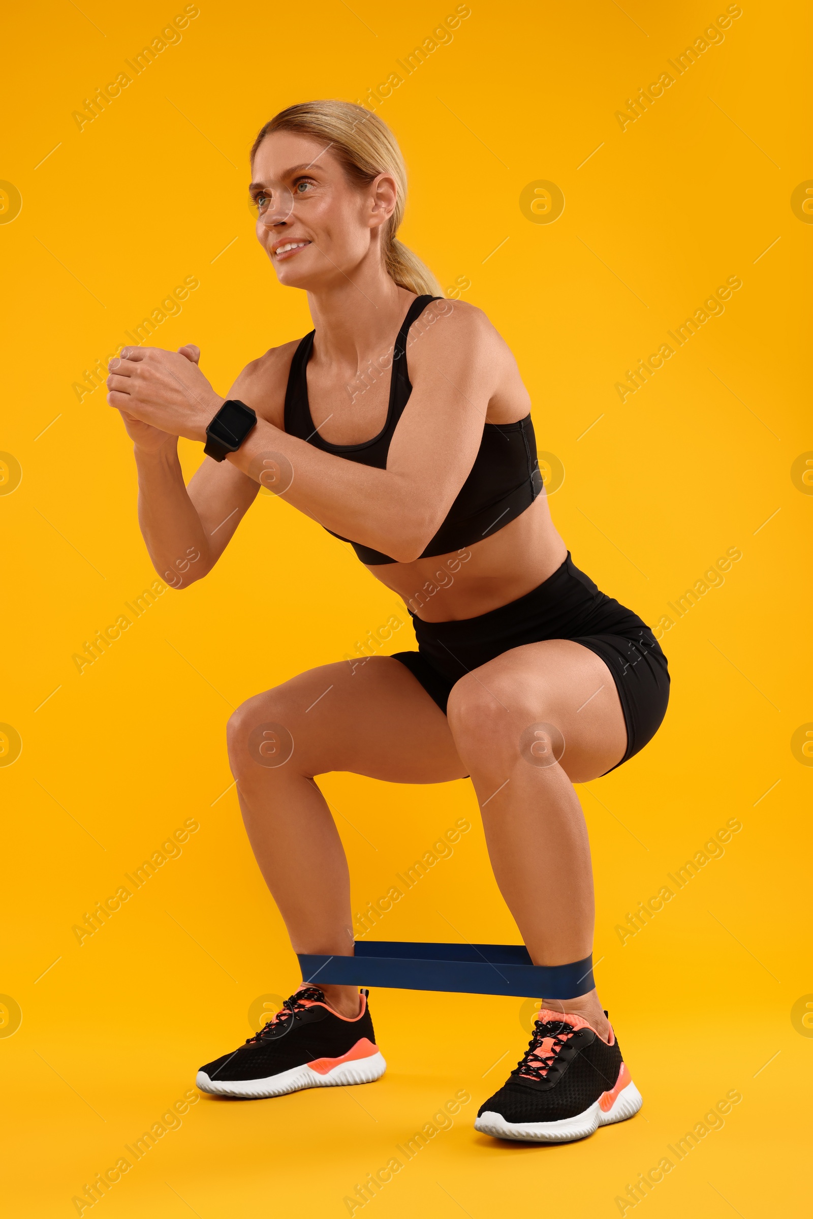 Photo of Woman exercising with elastic resistance band on orange background, low angle view