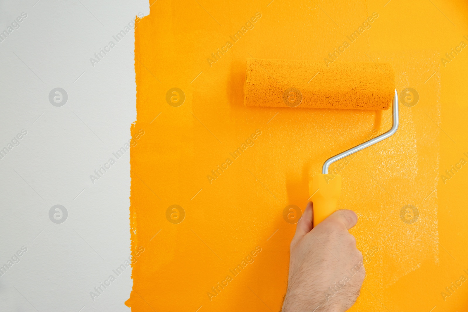 Photo of Man painting white wall with yellow dye, closeup. Interior renovation