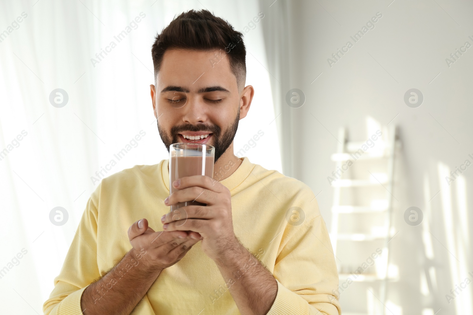 Photo of Young man drinking chocolate milk in room