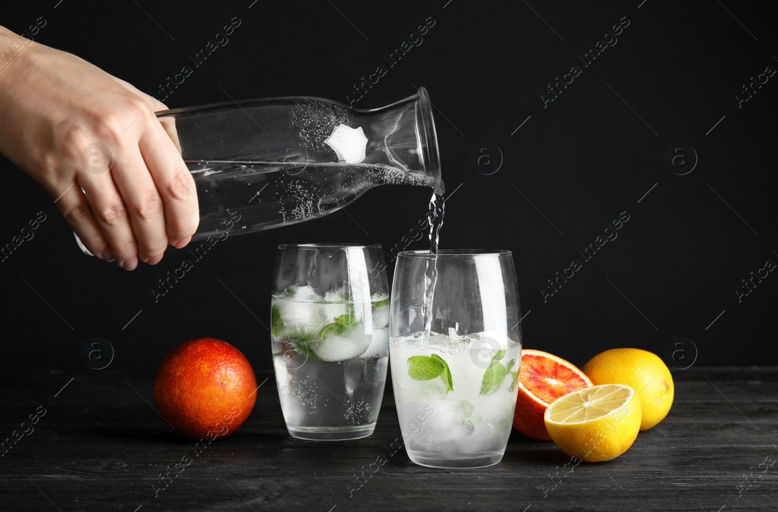 Photo of Woman pouring water into glass with ice cubes on table against black background