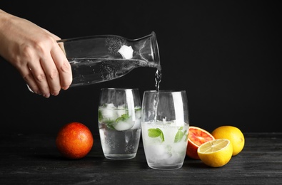 Woman pouring water into glass with ice cubes on table against black background