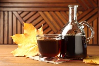 Photo of Bottle and glass of tasty maple syrup on wooden table