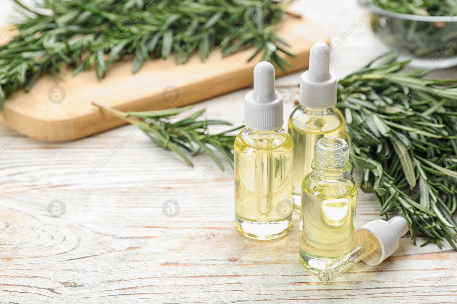 Photo of Bottles of rosemary essential oil on white wooden table. Space for text