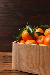 Photo of Fresh tangerines with green leaves in crate on wooden table, closeup