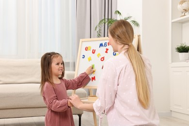 Photo of Mom teaching her daughter alphabet with magnetic letters at home