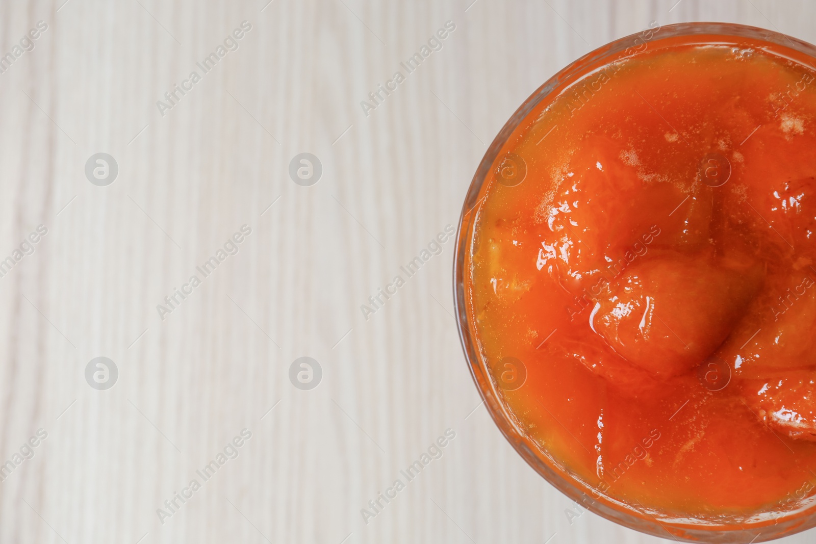 Photo of Dessert bowl with delicious apricot jam on white wooden table, top view. Space for text