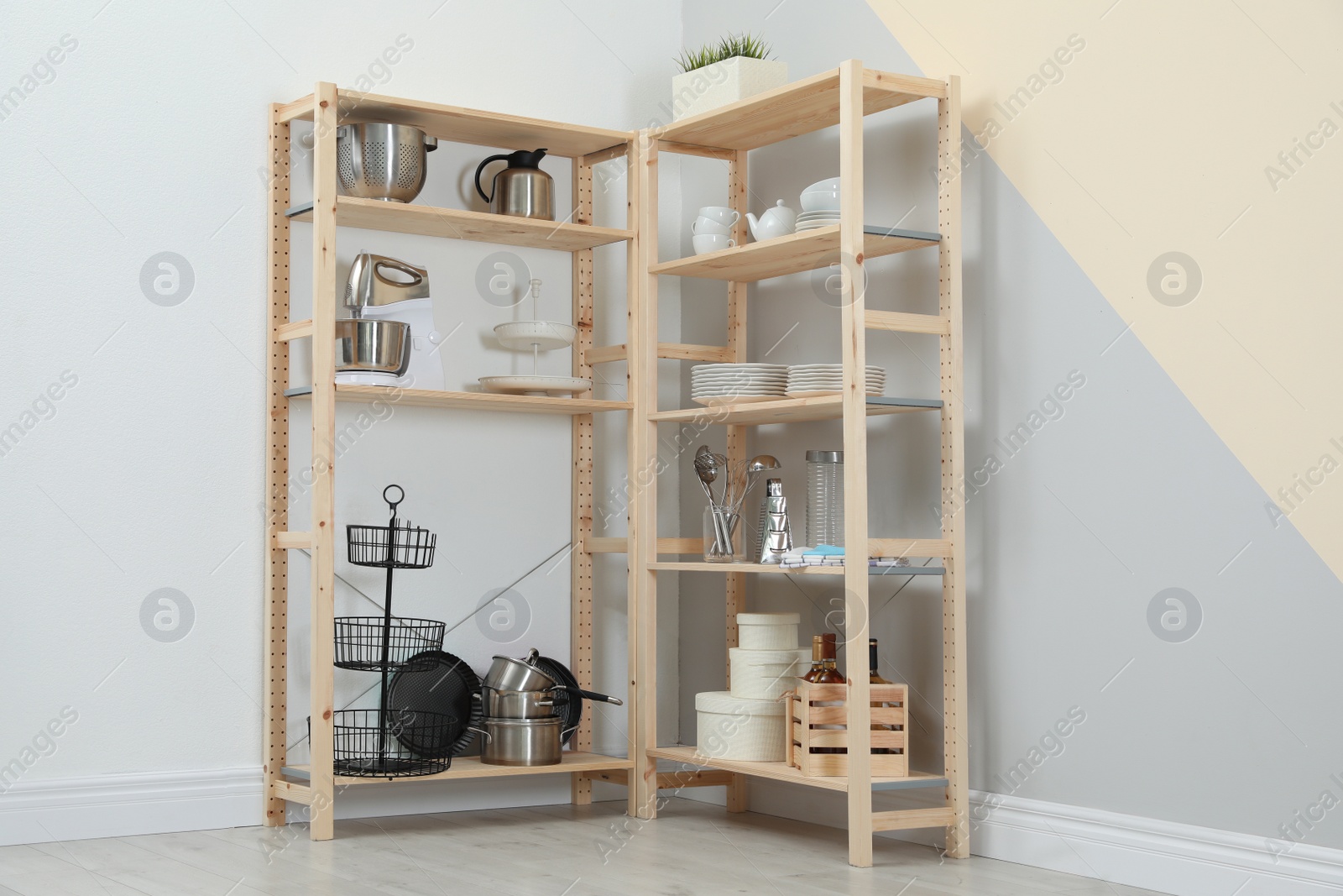 Photo of Wooden shelving units with kitchenware near color wall. Stylish room interior