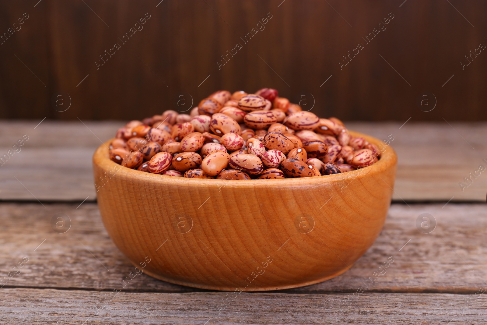 Photo of Bowl with dry kidney beans on old wooden table, closeup