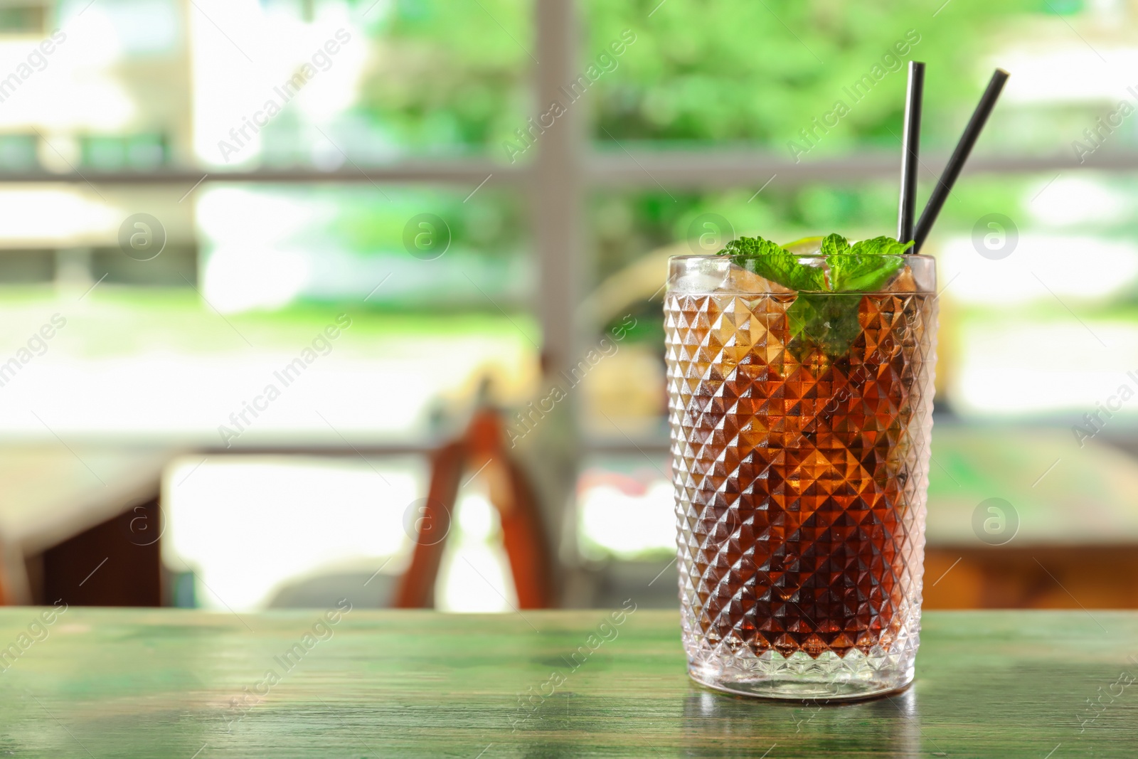 Photo of Glass of delicious cocktail with ice on table in bar