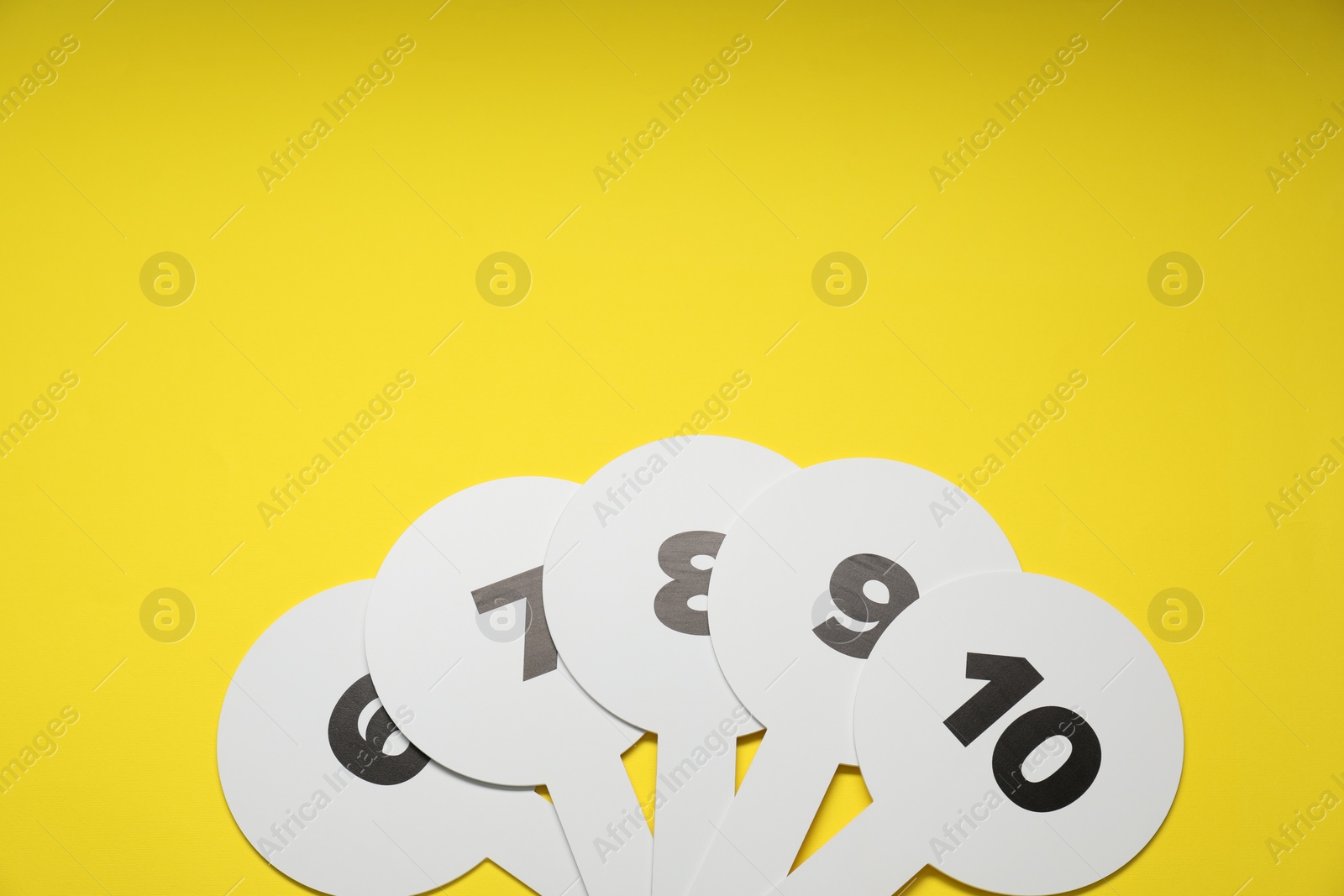 Photo of Auction paddles with numbers on yellow background, flat lay. Space for text