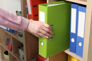 Woman taking binder office folder from shelving unit indoors, closeup