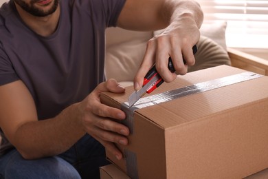 Man using utility knife to open parcel at home, closeup