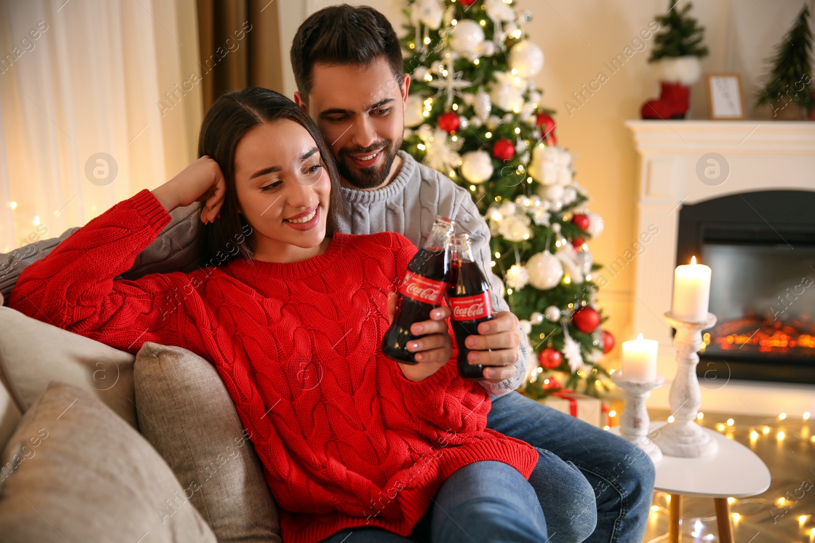 Photo of MYKOLAIV, UKRAINE - JANUARY 27, 2021: Young couple holding bottles of Coca-Cola in room decorated for Christmas