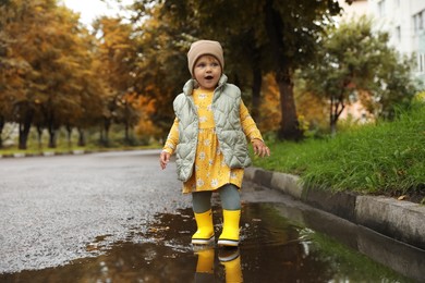 Photo of Cute little girl standing in puddle outdoors