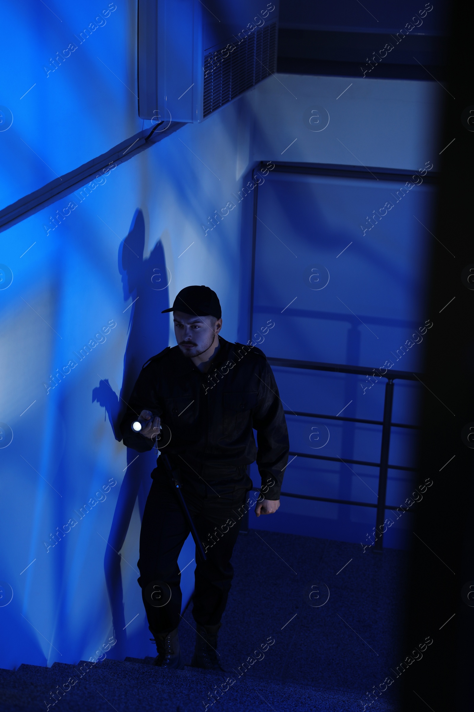 Photo of Male security guard with flashlight going up stairs in darkness