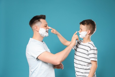 Happy dad and son with shaving foam on faces against blue background