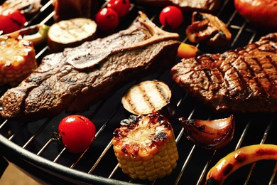 Photo of Fresh grilled meat steaks and vegetables on barbecue grate, closeup