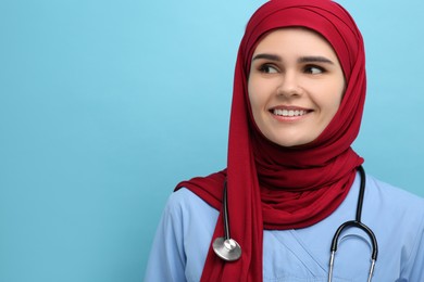 Photo of Muslim woman wearing hijab and medical uniform with stethoscope on light blue background, space for text