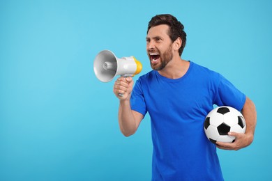 Photo of Emotional sports fan with soccer ball and megaphone on light blue background, space for text