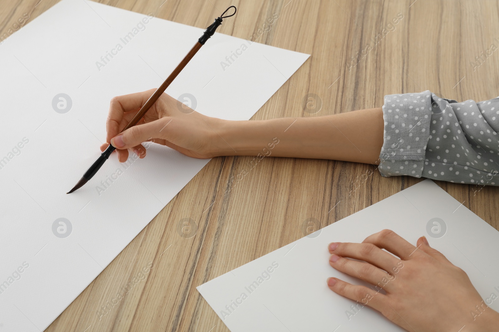 Photo of Woman painting with watercolor on blank paper at wooden table, closeup