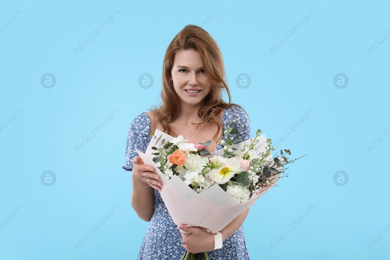 Photo of Happy woman with bouquet of beautiful flowers on light blue background