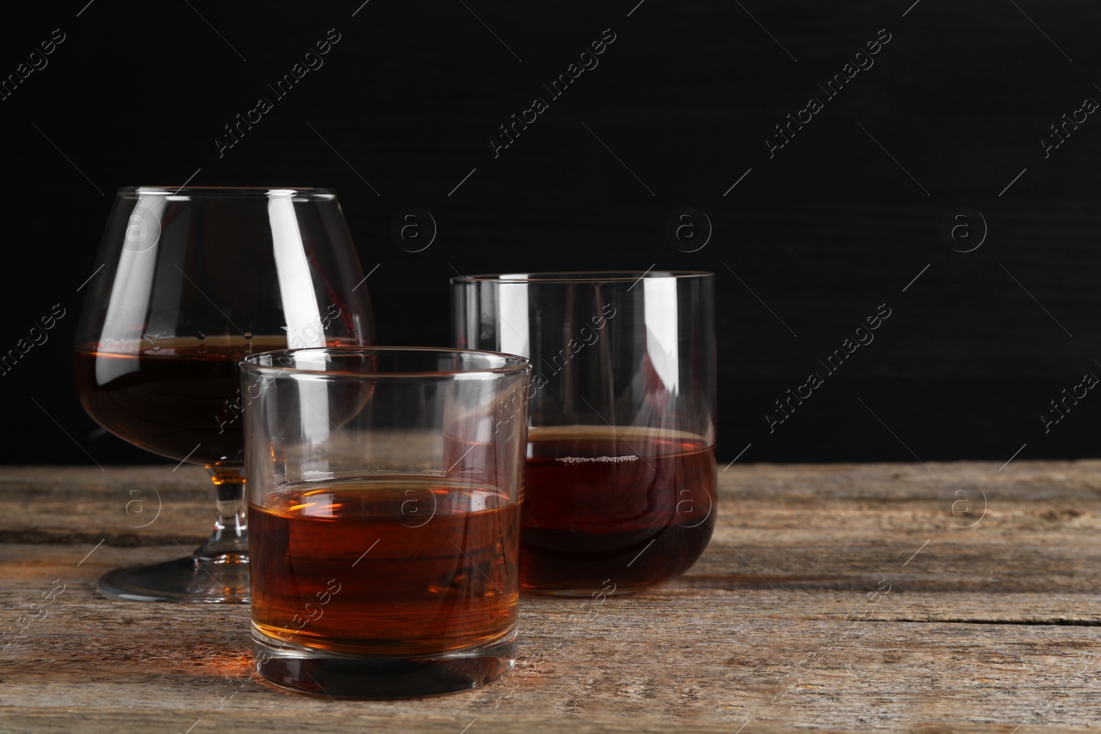 Photo of Different delicious liqueurs in glasses on wooden table, space for text