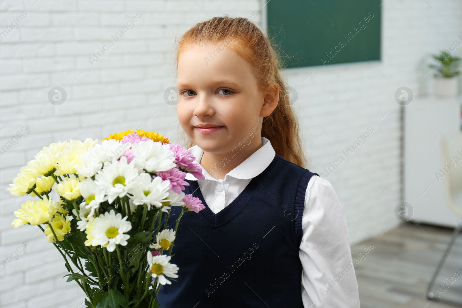 Photo of Happy schoolgirl with bouquet in classroom. Teacher's day