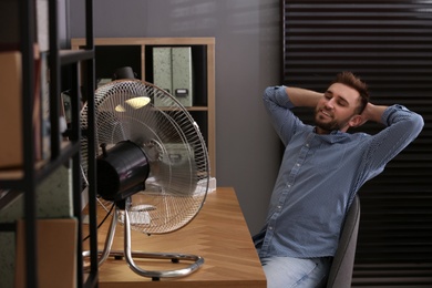 Man enjoying air flow from fan at workplace