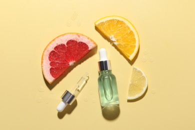 Photo of Bottle of cosmetic serum and sliced citrus fruits on yellow background, flat lay