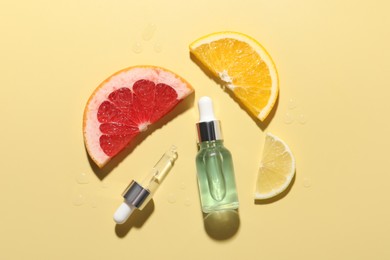 Bottle of cosmetic serum and sliced citrus fruits on yellow background, flat lay