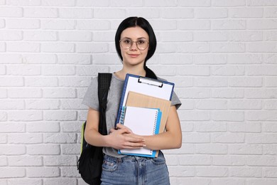 Student with notebooks, clipboard and backpack near white brick wall