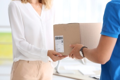 Photo of Young woman receiving parcel from courier in office
