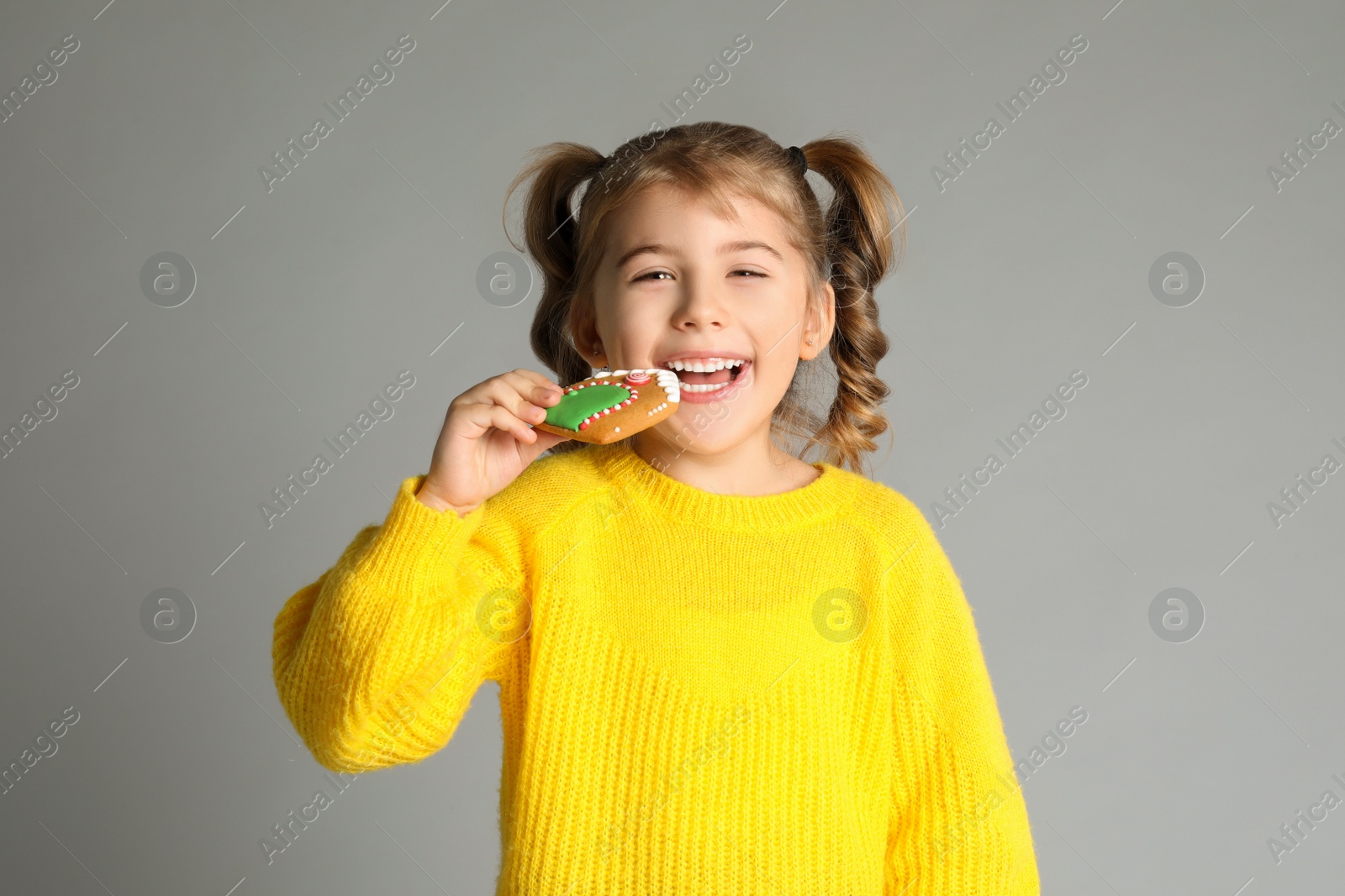 Photo of Cute little girl with Christmas gingerbread cookie on light grey background