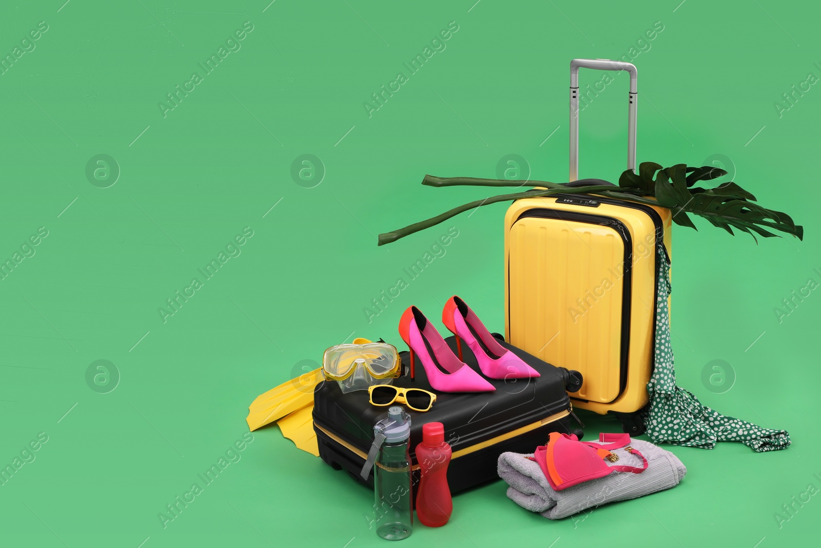 Photo of Suitcases, beach accessories and tropical leaves on green background, space for text. Summer vacation