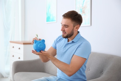 Photo of Young man with piggy bank on sofa in living room