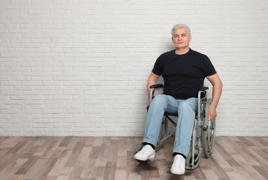Photo of Senior man in wheelchair near brick wall indoors. Space for text