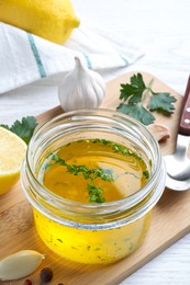 Photo of Jar with lemon sauce and ingredients on white wooden table, closeup. Delicious salad dressing