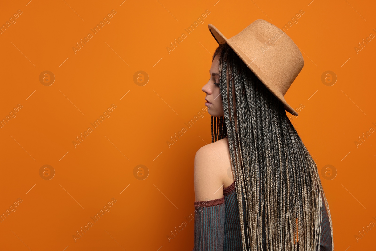 Photo of Beautiful woman with long african braids and hat on orange background, space for text