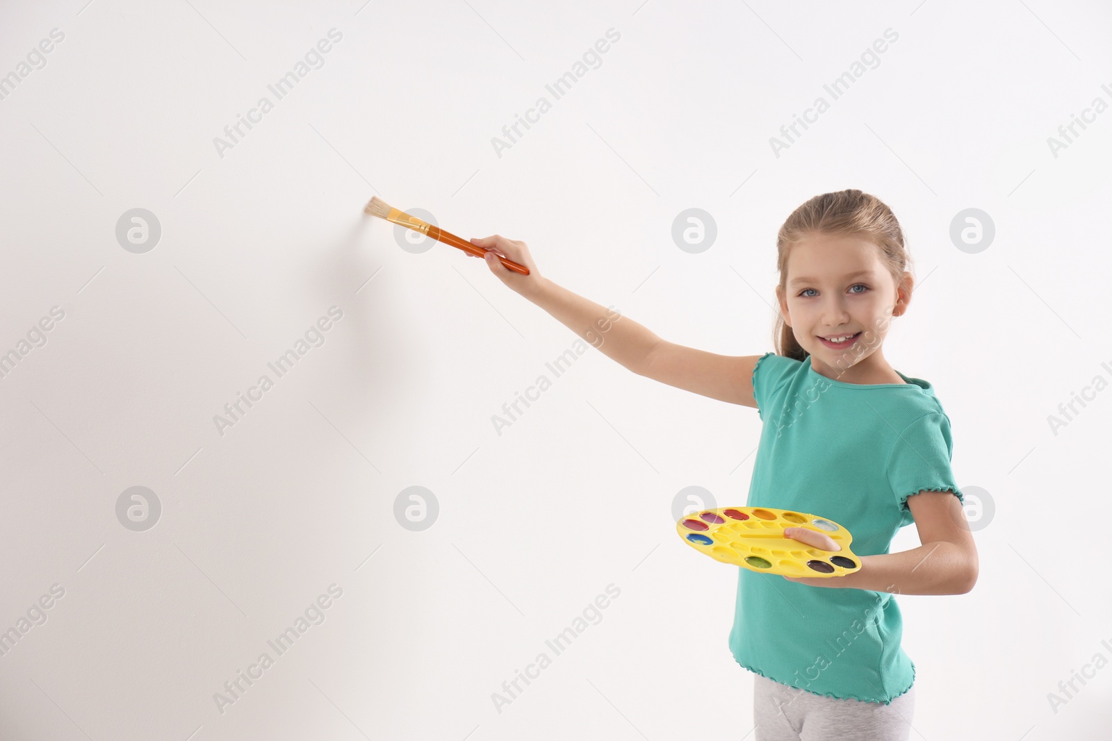 Photo of Little child painting on white wall indoors. Space for text