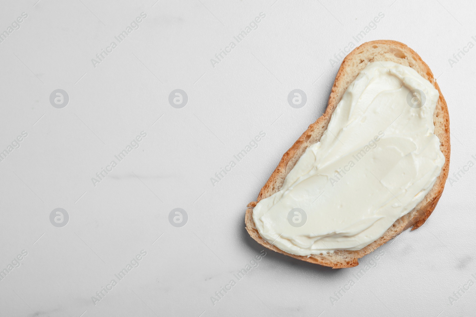 Photo of Slice of bread with tasty cream cheese on white marble table, top view. Space for text