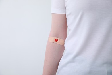 Photo of Blood donation concept. Woman with adhesive plaster on arm against white background, closeup. Space for text