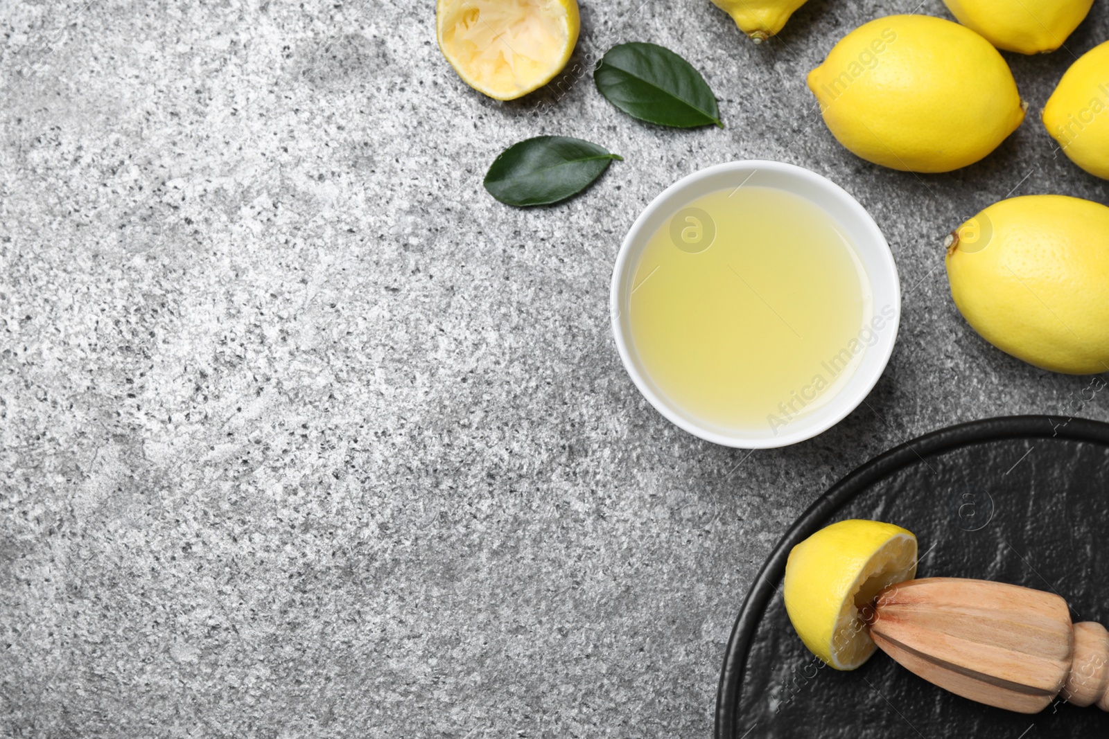 Photo of Flat lay composition with freshly squeezed lemon juice and reamer on grey table. Space for text