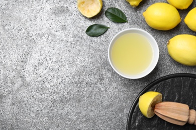 Flat lay composition with freshly squeezed lemon juice and reamer on grey table. Space for text